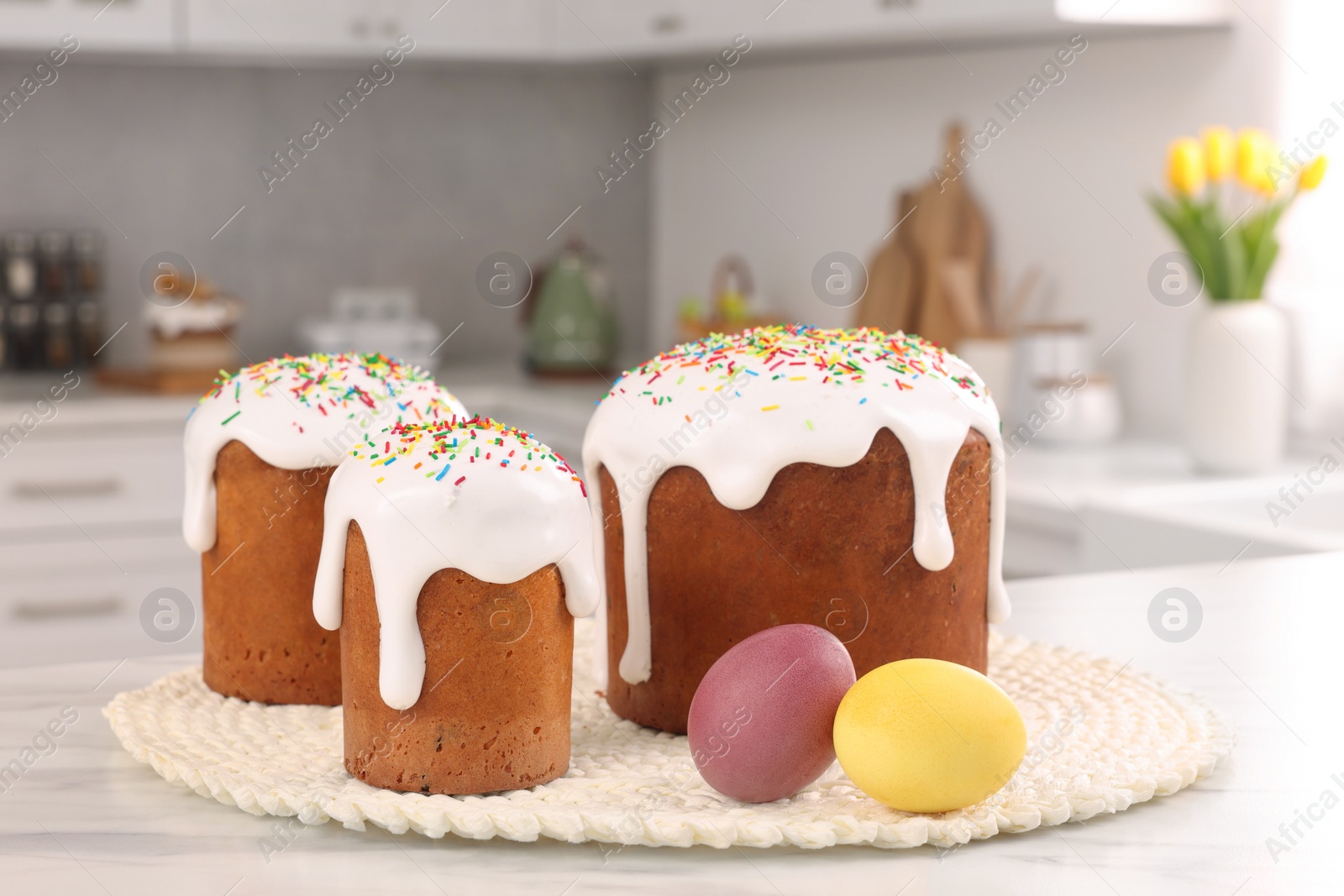 Photo of Delicious Easter cakes with sprinkles and painted eggs on white table in kitchen