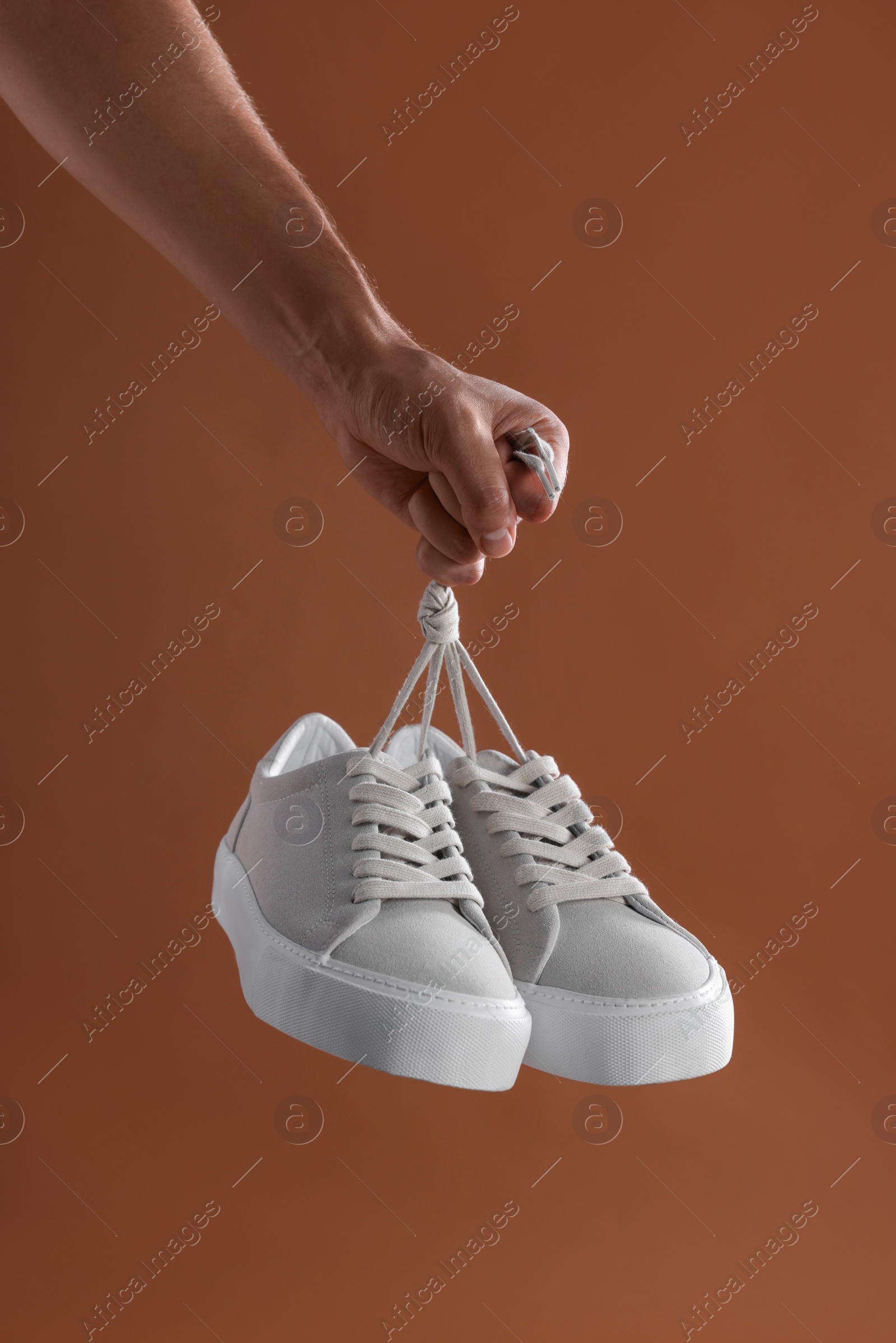 Photo of Man holding stylish sneakers on brown background, closeup