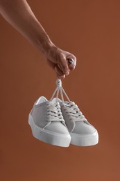 Man holding stylish sneakers on brown background, closeup