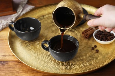 Photo of Turkish coffee. Woman pouring brewed beverage from cezve into cup at wooden table, closeup