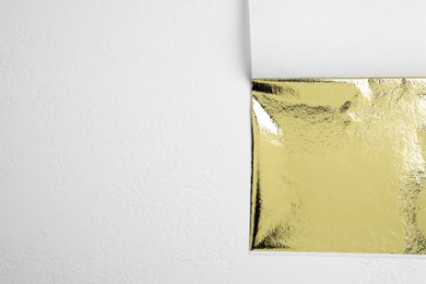 Photo of Edible gold leaf sheet on white background, top view. Space for text