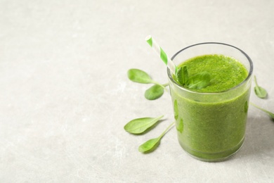 Photo of Green juice and fresh spinach leaves on light grey table. Space for text