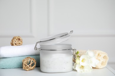 Jar of salt scrub, freesia flowers and towels on white table