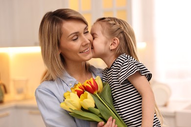 Little daughter kissing and congratulating her mom with Mother`s Day at home. Woman holding bouquet of beautiful tulips