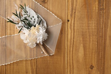 Stylish boutonniere and ribbon on wooden table, top view. Space for text