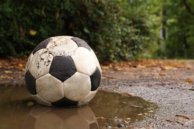 Dirty soccer ball in muddy puddle, space for text