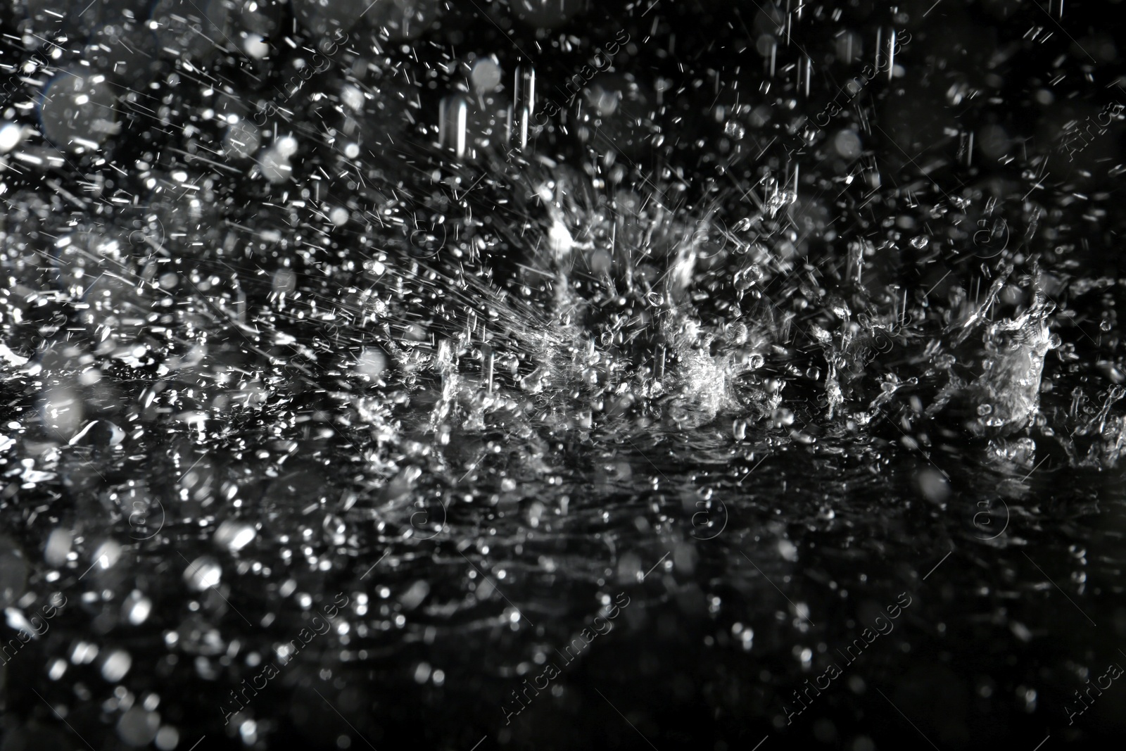 Photo of Heavy rain falling down into puddle on dark background