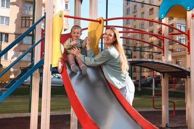 Photo of Happy nanny and cute little boy on slide at playground