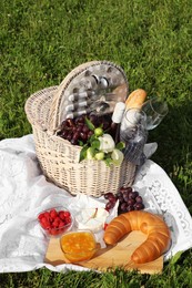 Photo of Picnic blanket with tasty food, flowers, basket and cider on green grass outdoors