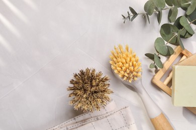 Cleaning brushes, soap bars and eucalyptus leaves on white table, flat lay. Space for text