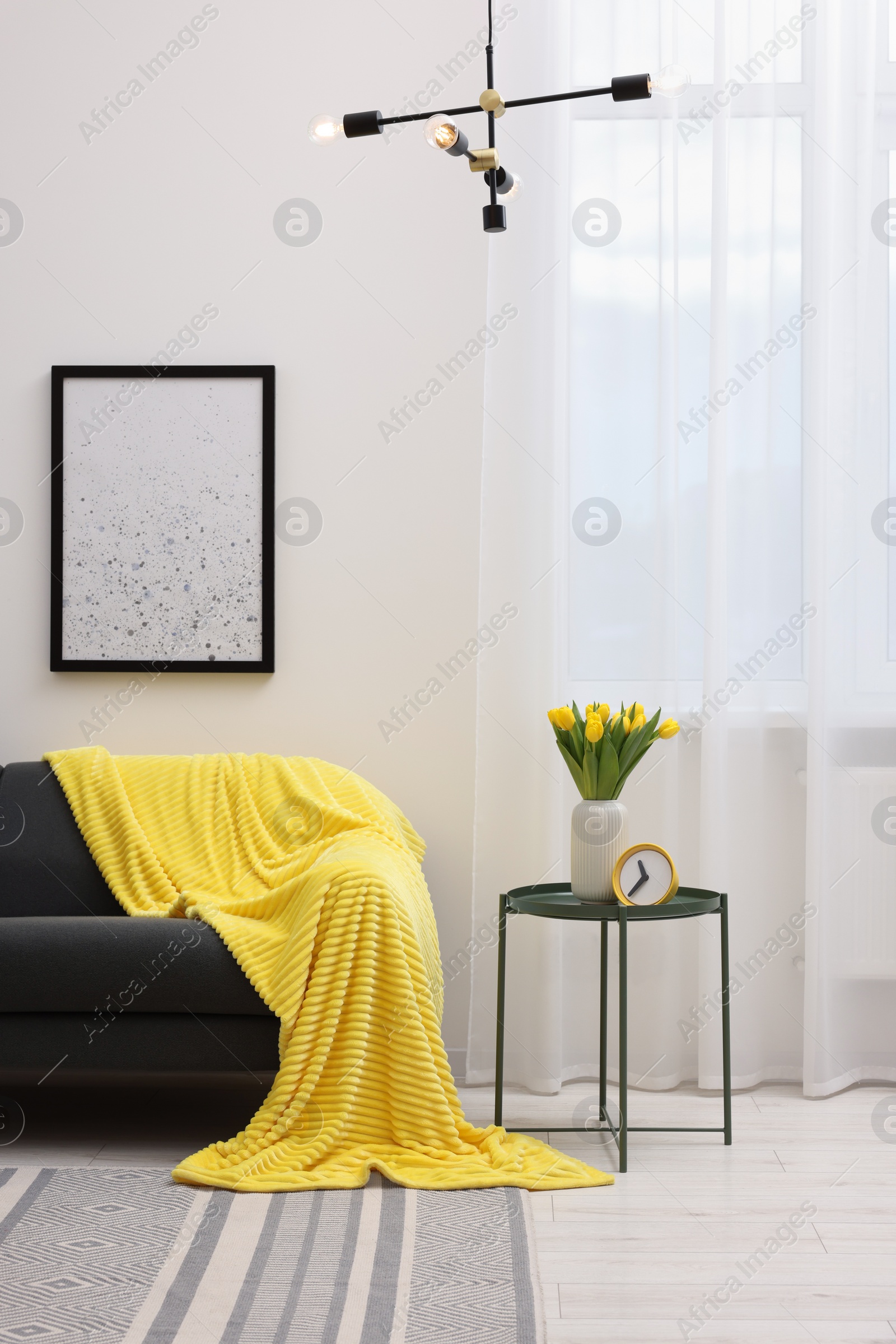 Photo of Spring atmosphere. Stylish living room interior with comfortable furniture and bouquet of beautiful yellow tulips