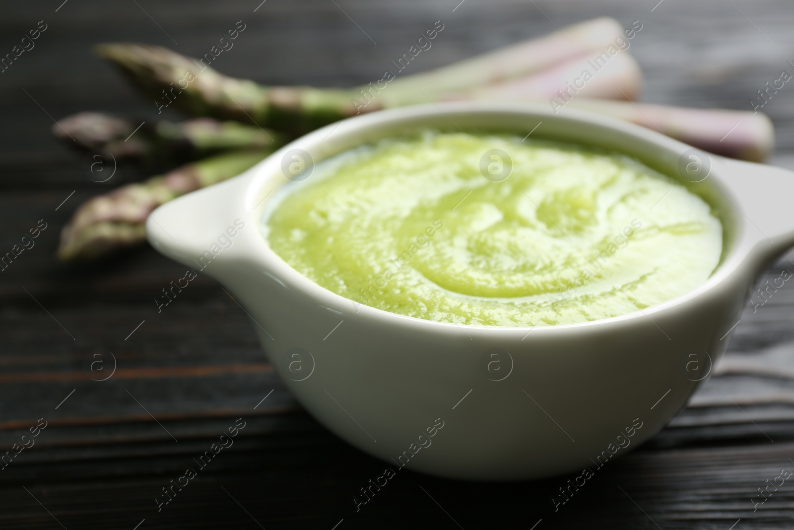 Photo of Delicious asparagus soup in bowl on black wooden table