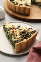 Piece of delicious homemade spinach quiche on light gray table, closeup