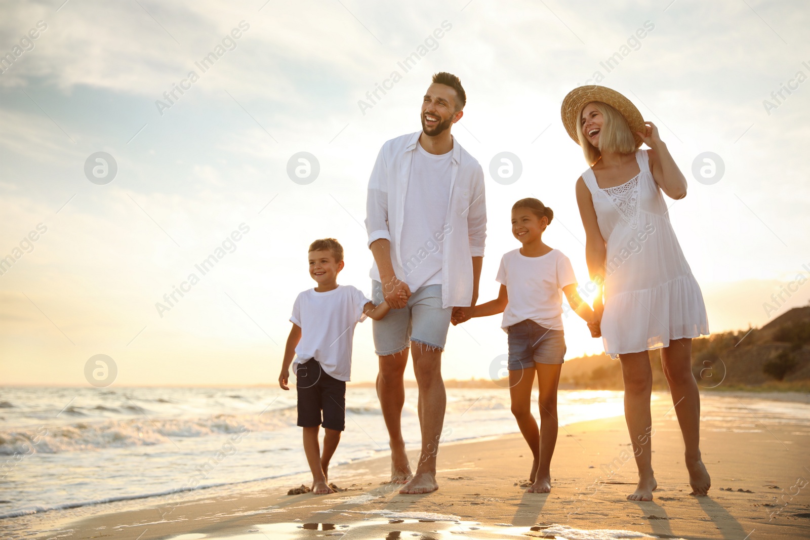 Photo of Happy family walking on sandy beach near sea at sunset