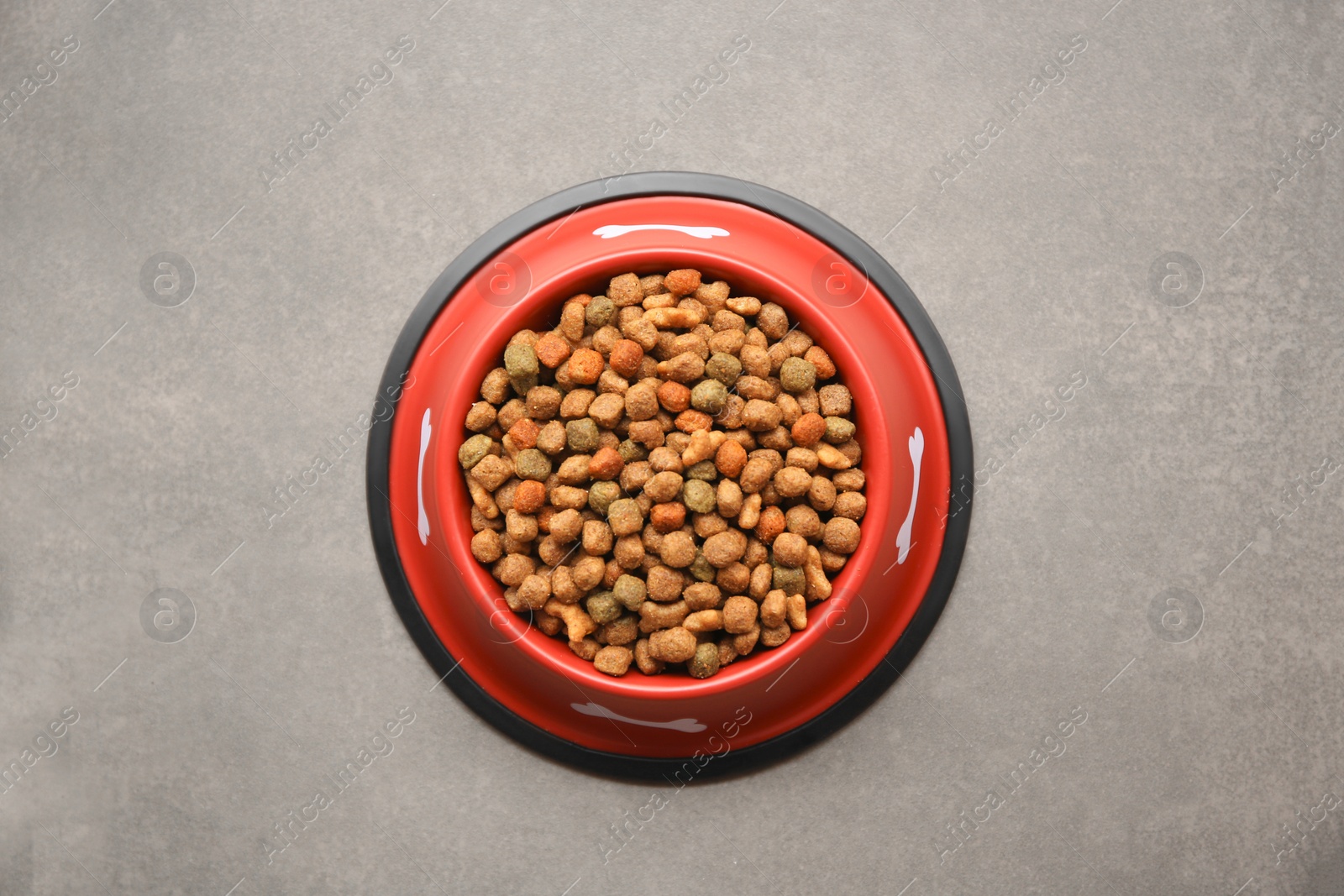 Photo of Dry dog food in feeding bowl on beige floor, top view