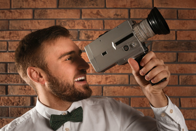 Young man with vintage video camera near brick wall