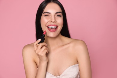 Photo of Young woman with beautiful makeup holding glossy lipstick on pink background