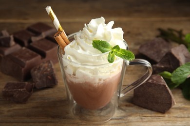 Photo of Glass cup of delicious hot chocolate with whipped cream and mint on wooden table