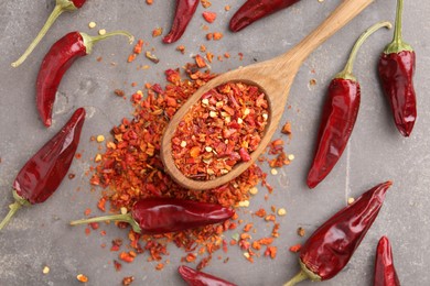 Photo of Chili pepper flakes, pods and spoon on grey table, flat lay