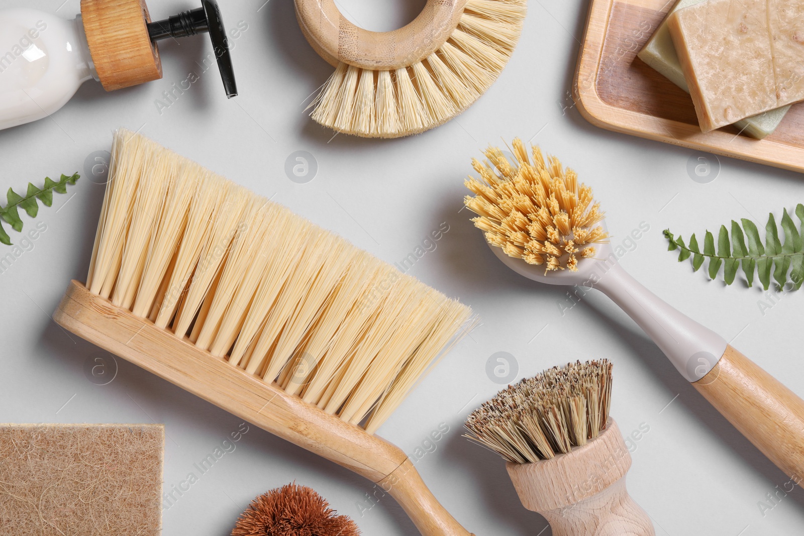 Photo of Cleaning brushes, soap, dispenser and fern leaves on grey background, flat lay