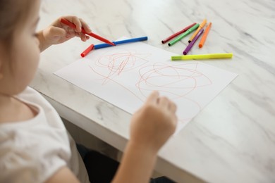 Photo of Little girl drawing with marker at white marble table, closeup
