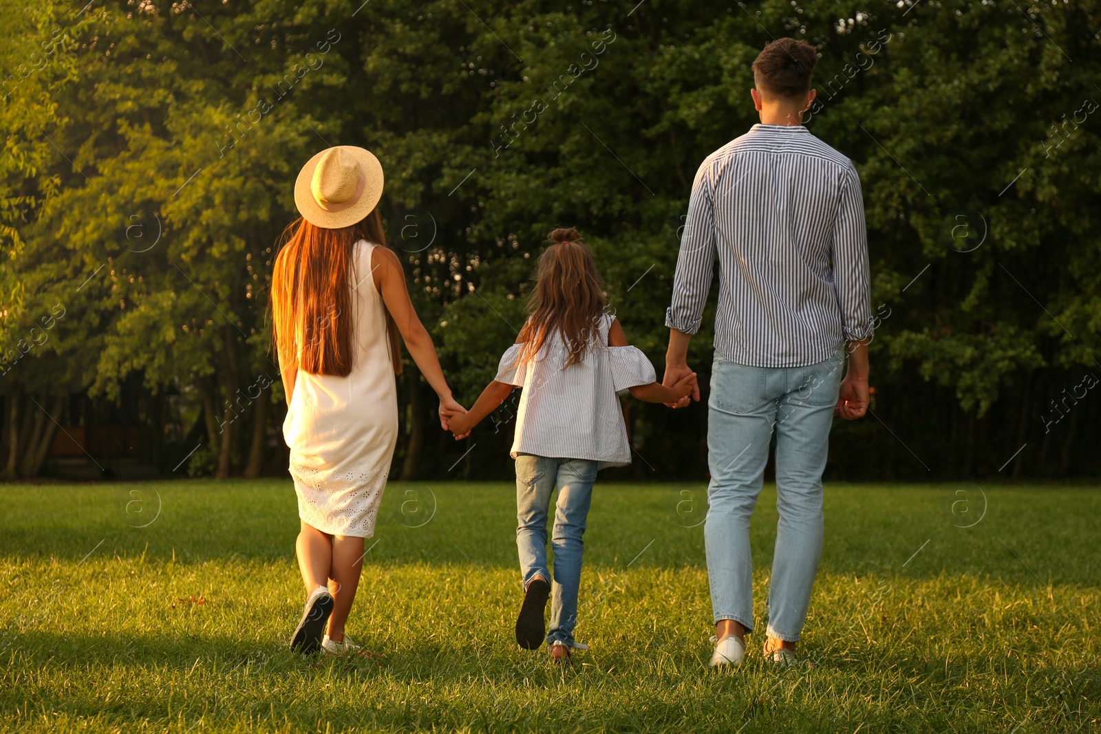 Photo of Little girl and her parents holding hands in park. Happy family