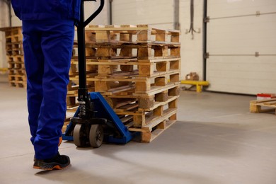 Image of Worker moving wooden pallets with manual forklift in warehouse, closeup