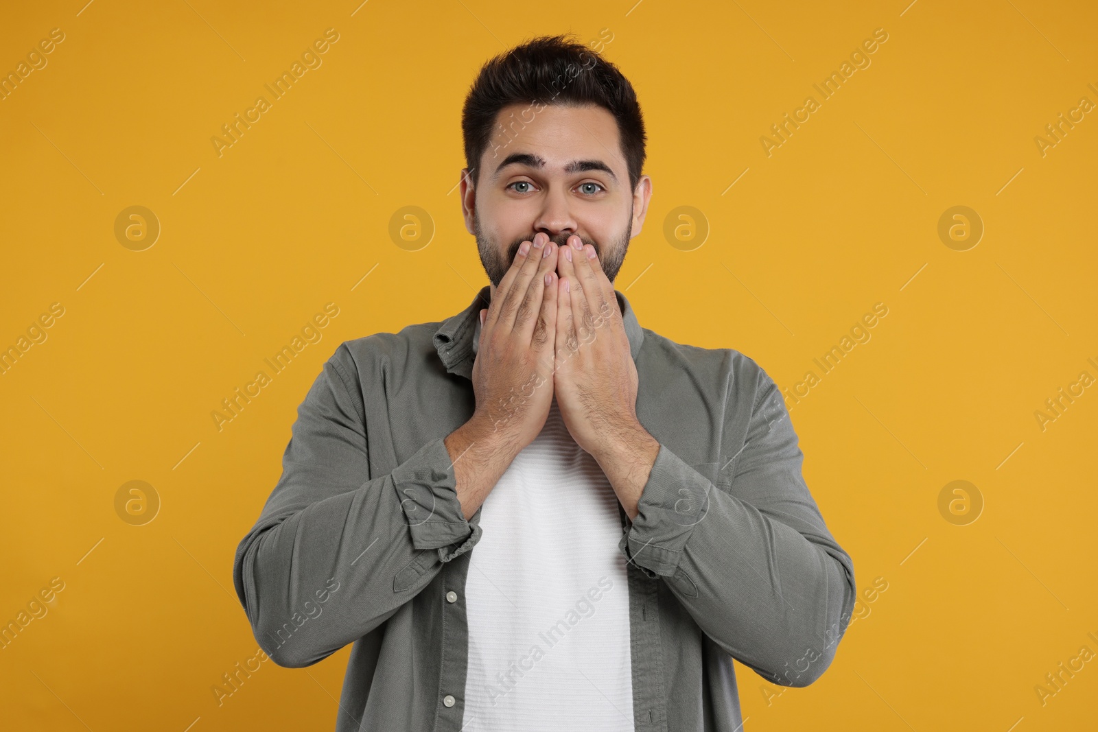 Photo of Embarrassed man covering mouth with hands on orange background