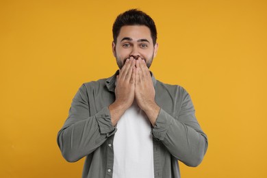 Photo of Embarrassed man covering mouth with hands on orange background