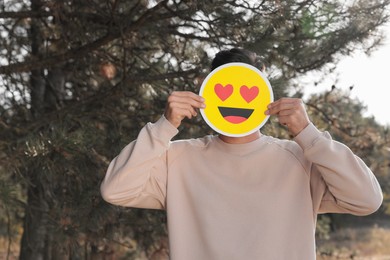 Photo of Man hiding emotions using card with drawn smiling face in forest