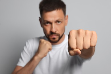 Photo of Man throwing punch against grey background, focus on fist. Space for text