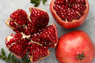 Fresh pomegranates and green leaves on grey textured table, flat lay