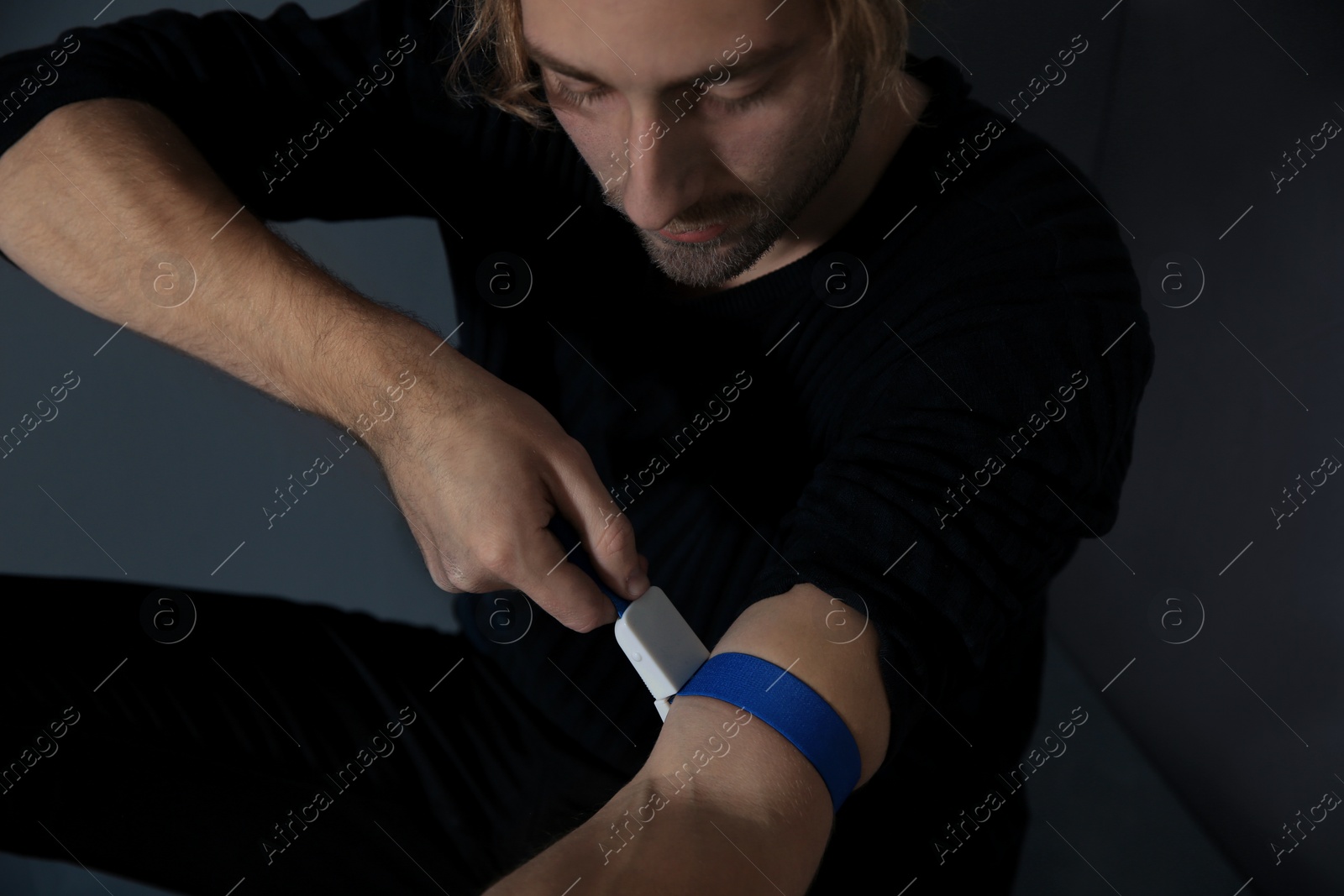 Photo of Male drug addict preparing hand for injection on grey background