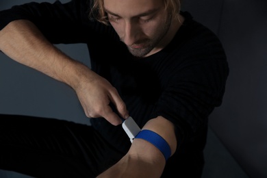 Male drug addict preparing hand for injection on grey background