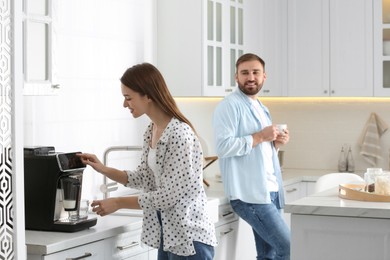 Beautiful young woman and her boyfriend using modern coffee machine in kitchen