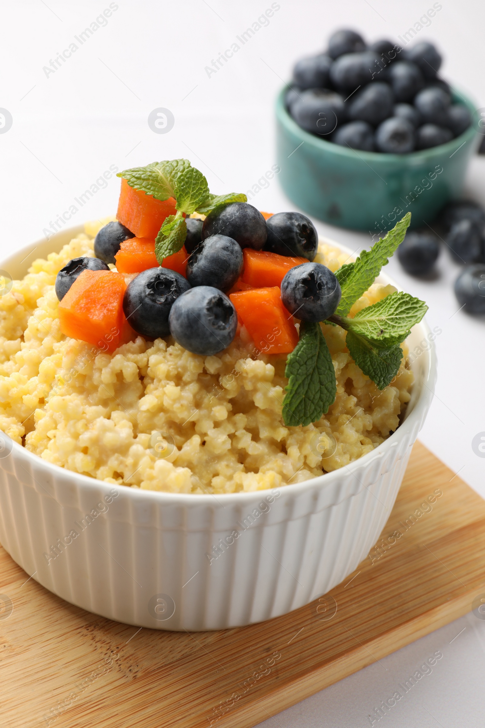 Photo of Tasty millet porridge with blueberries, pumpkin and mint in bowl on white table, closeup