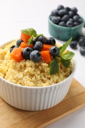 Photo of Tasty millet porridge with blueberries, pumpkin and mint in bowl on white table, closeup