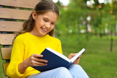 Image of Happy little girl reading book in park 