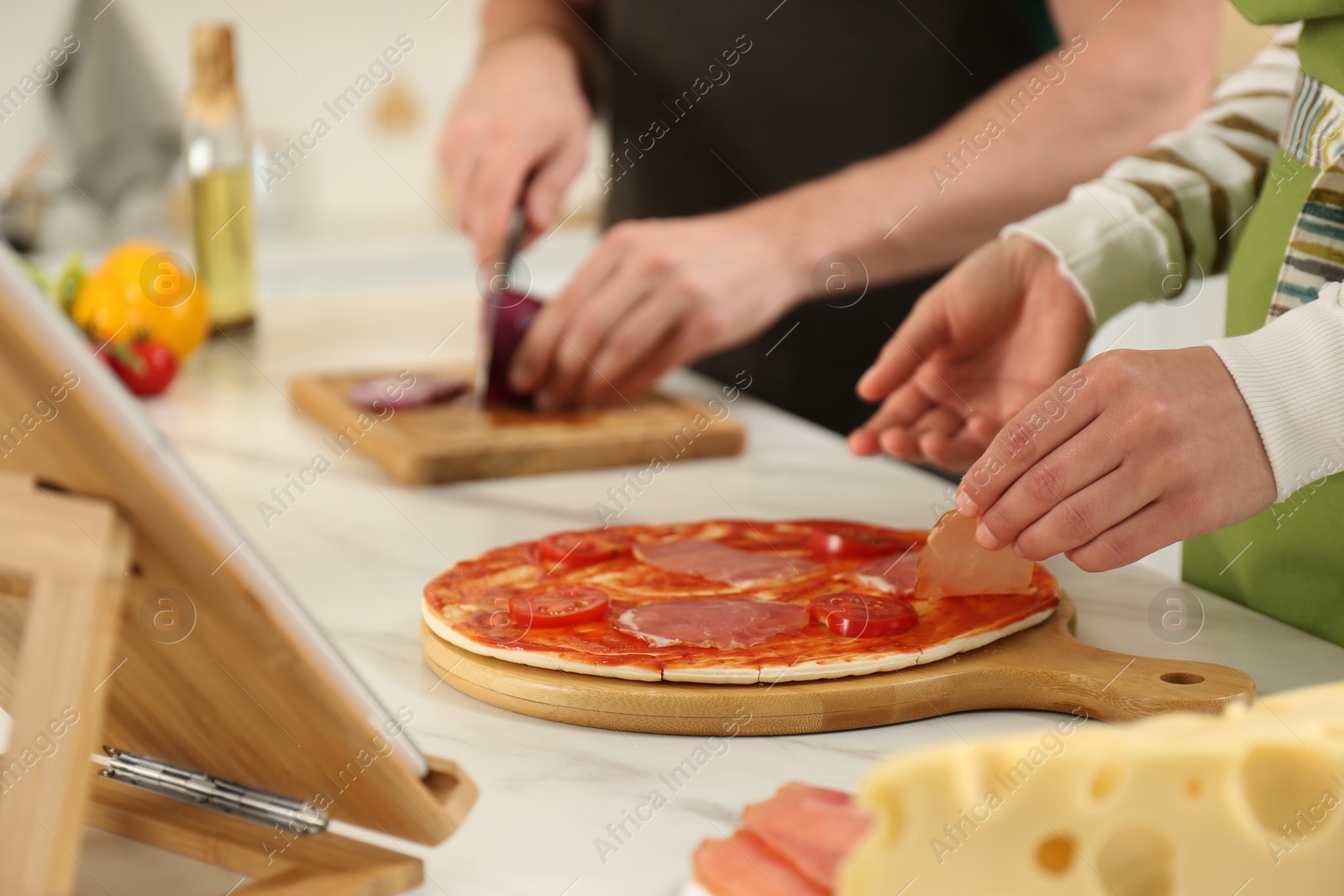 Photo of Couple making pizza together while watching online cooking course via tablet in kitchen, closeup