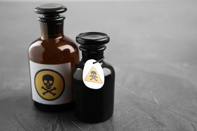 Photo of Glass bottles of poison with warning signs on grey stone table. Space for text