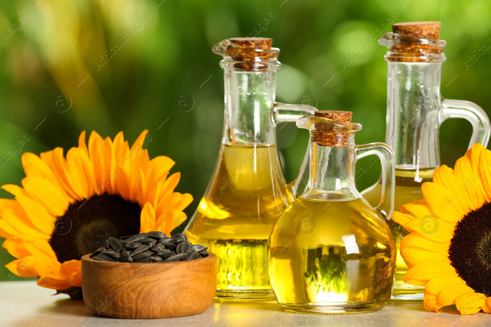 Photo of Sunflower cooking oil, seeds and yellow flowers on light grey table outdoors, closeup