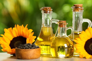 Photo of Sunflower cooking oil, seeds and yellow flowers on light grey table outdoors, closeup