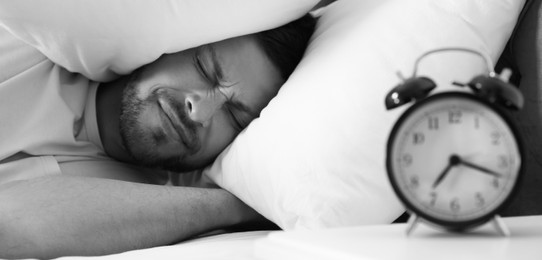 Image of Emotional man covering ears with pillows at home in morning, selective focus. Black and white photography