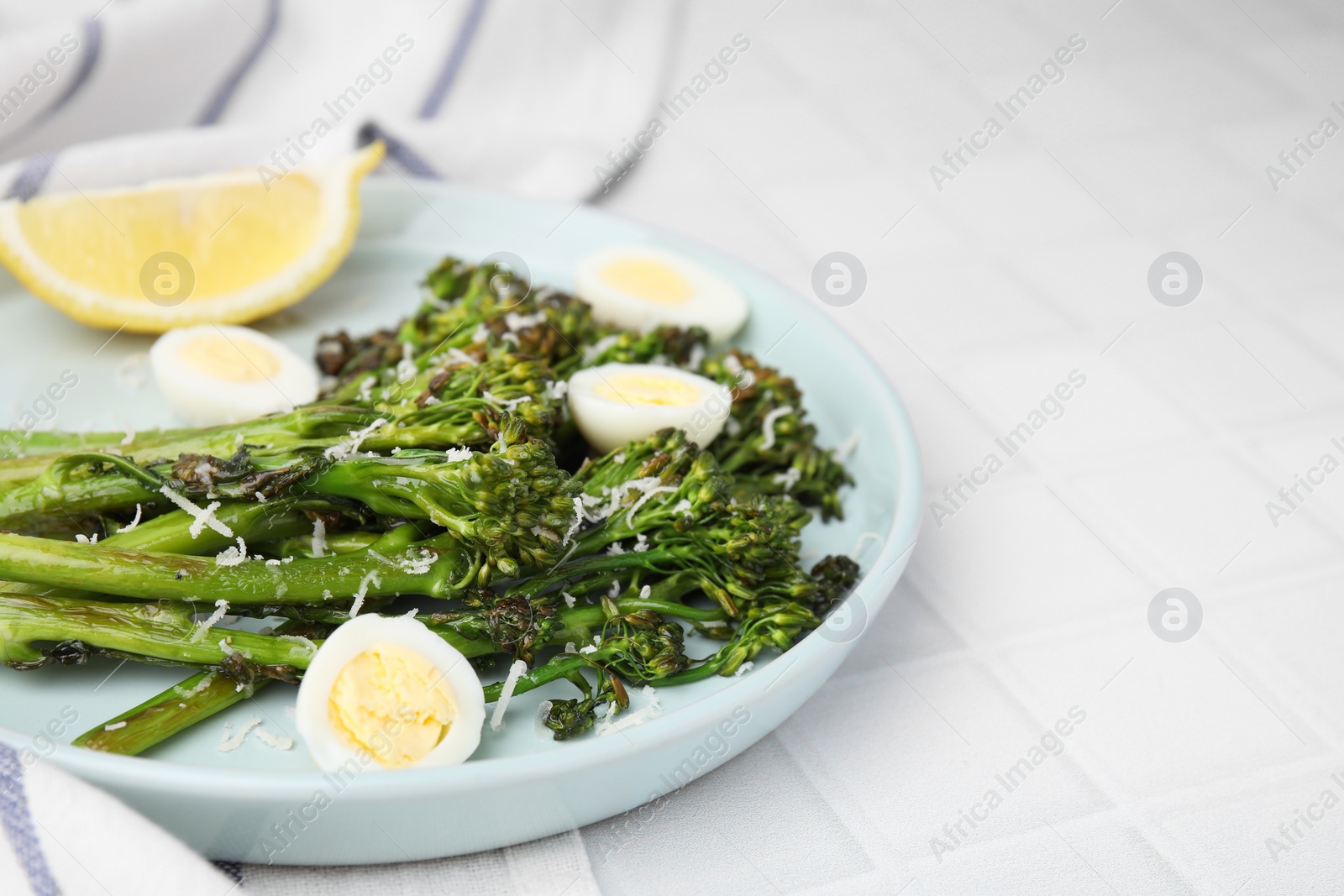 Photo of Tasty cooked broccolini with cheese, quail eggs and lemon on white tiled table, closeup. Space for text