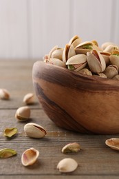 Photo of Tasty pistachios in bowl on wooden table, closeup