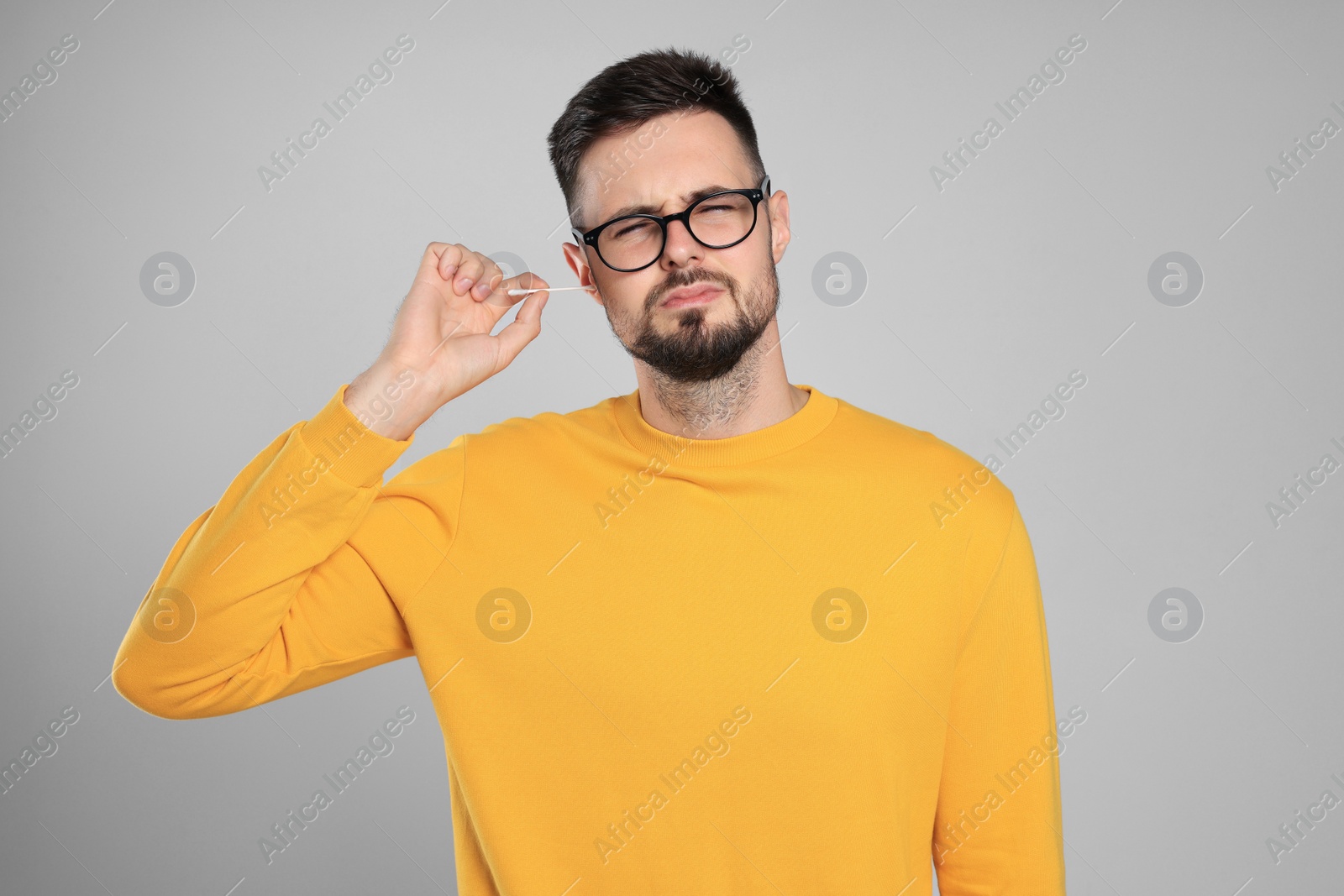 Photo of Young man cleaning ear with cotton swab on light grey background