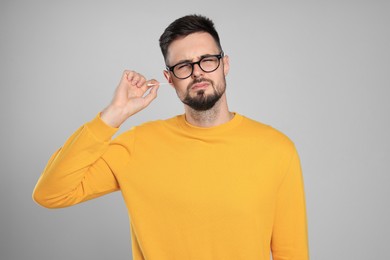 Young man cleaning ear with cotton swab on light grey background