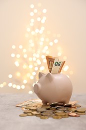 Piggy bank with euro banknote and coins on grey table against blurred lights, space for text