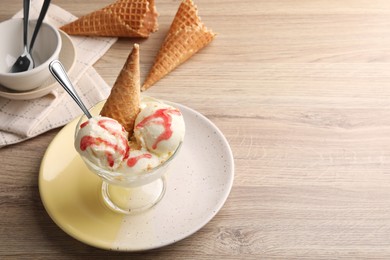 Photo of Delicious scoops of vanilla ice cream with wafer cone and strawberry topping in glass dessert bowl on wooden table, above view. Space for text