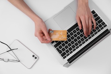 Photo of Woman with credit card using laptop for online shopping at white table, top view